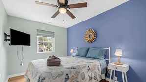 A bedroom with a bed, a ceiling fan, a TV, a window, and a wall decoration. - Lovely 3Br House,Beach Access,Sm Dogs,V384 (North Myrtle Beach)