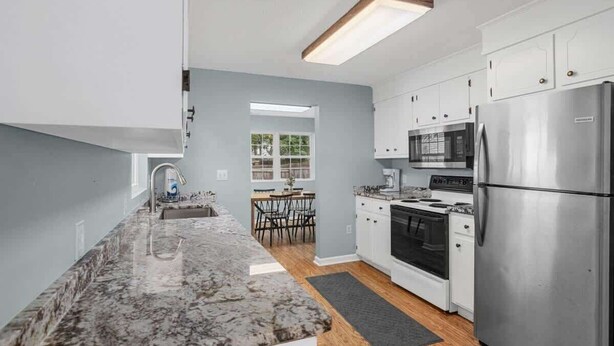 A modern kitchen with white cabinets, a granite countertop, stainless steel appliances, and a dining area with a table and chairs. - Lovely 3Br House,Beach Access,Sm Dogs,V384 (North Myrtle Beach)