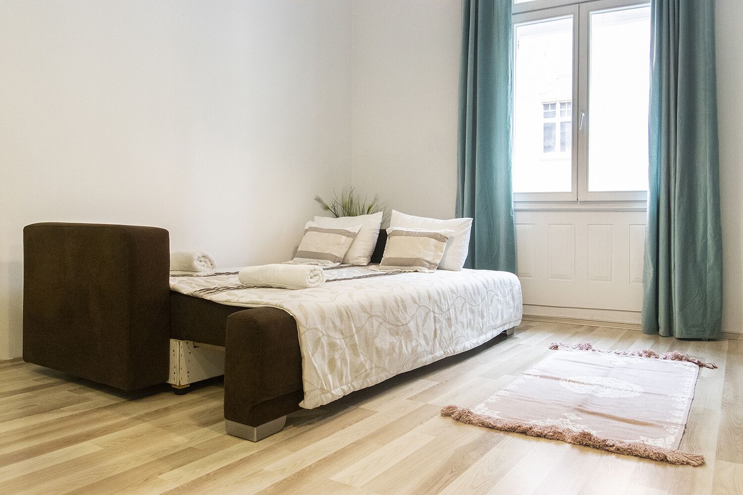 Un dormitorio con cama, una silla, una ventana con cortinas y suelo de madera.