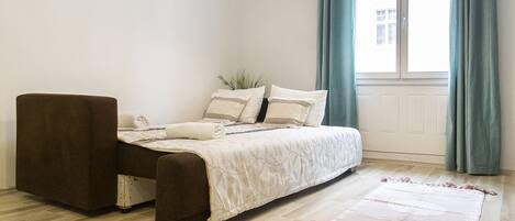 Un dormitorio con cama, una silla, una ventana con cortinas y suelo de madera.