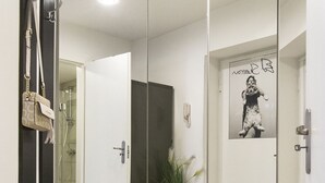 Um corredor com um guarda-roupa espelhado, uma porta que dá para um banheiro e um vaso de plantas.