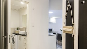 Cozinha moderna com máquina de lavar, área de jantar com mesa e cadeiras, e corredor com porta.