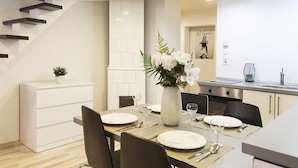 Uma cozinha moderna com armários brancos, um espaço de jantar com mesa posta para dois e uma escada com guarda-corrimão preto.