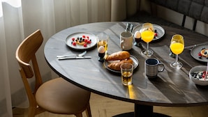 A dining area with a round table, two wooden chairs, a bench, and a TV mounted on the wall. - Ocean House Scheveningen (The Hague)