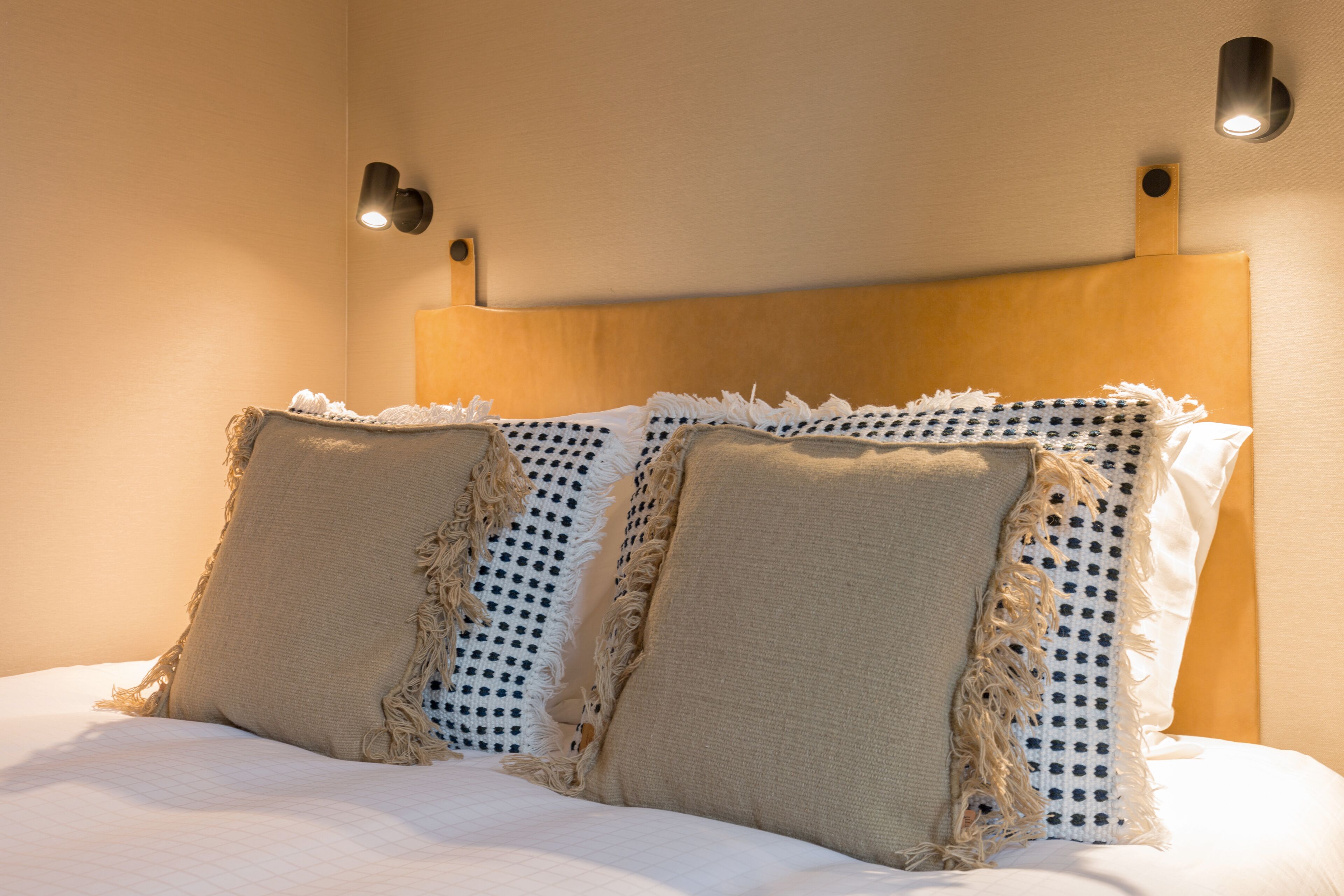 Una cama con cabecera de madera, dos almohadas y dos lámparas fijadas a la pared.