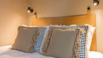 Una cama con cabecera de madera, dos almohadas y dos lámparas fijadas a la pared.