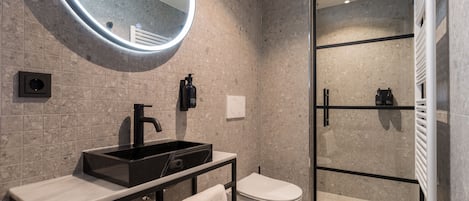 Moderni kylpyhuone, jossa on musta pesuallas, wc ja lasiseinällä varustettu suihku.