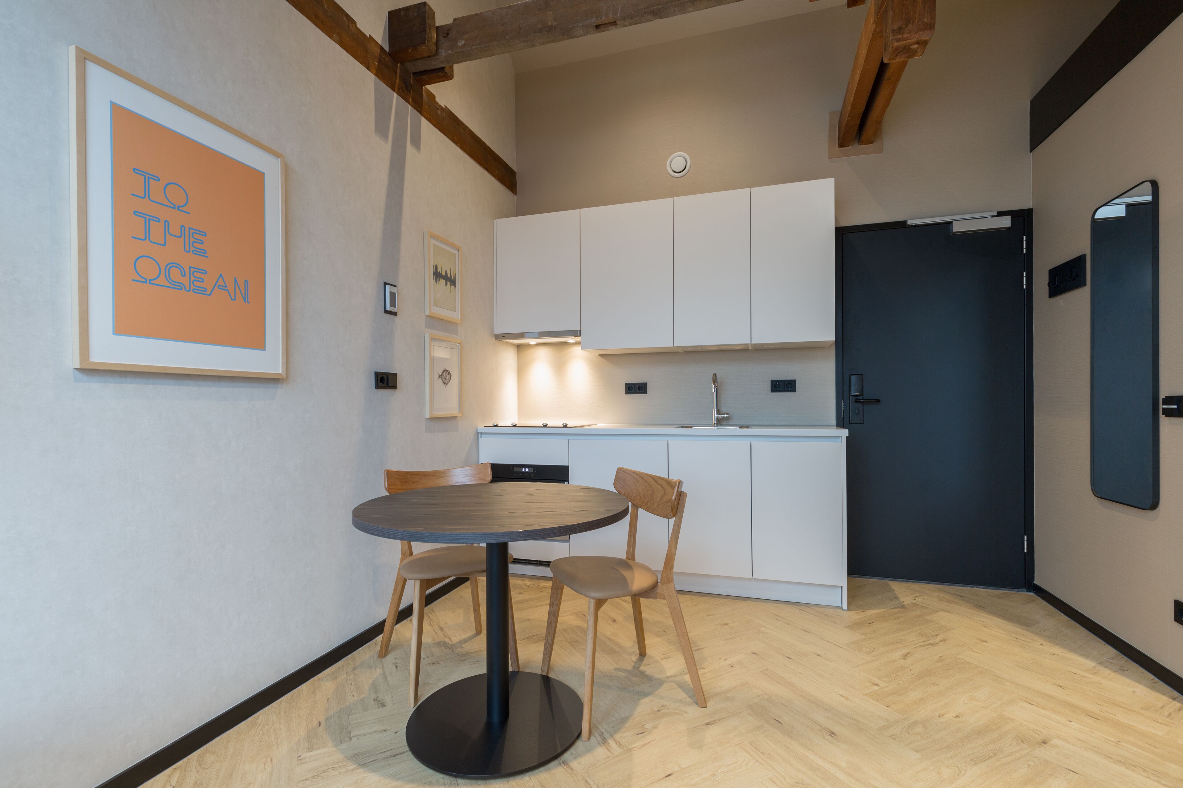 A modern kitchen with white cabinets, a round table with chairs, and a framed artwork on the wall.