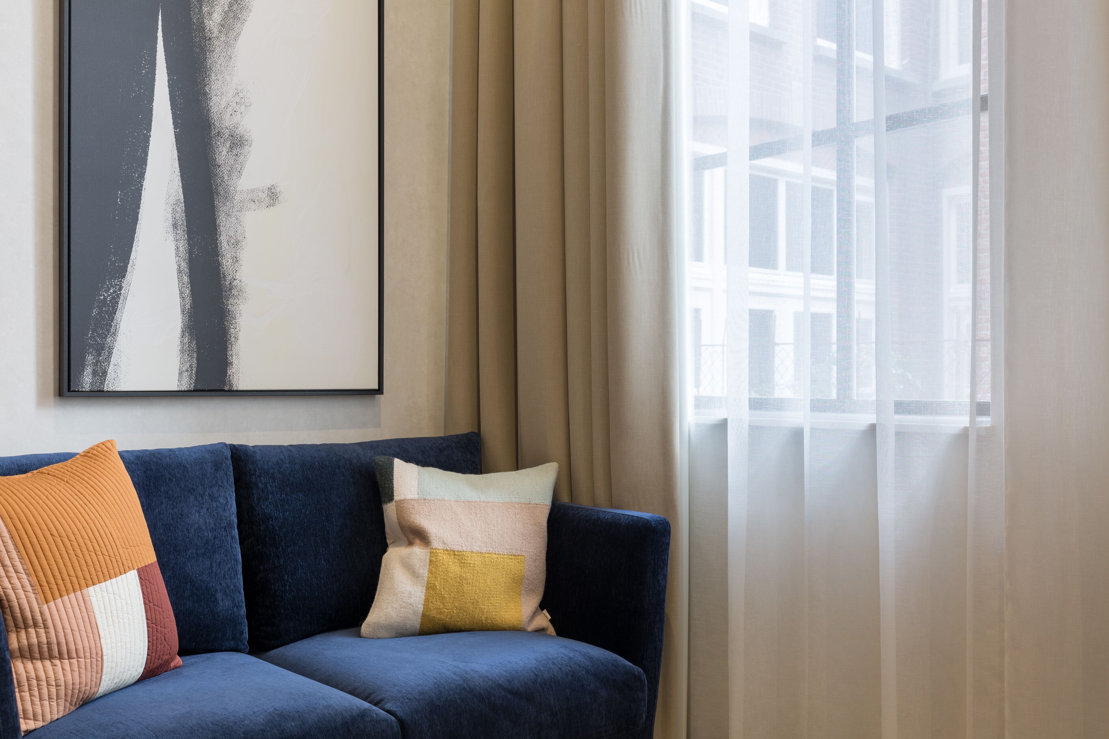 A modern living room with a blue sofa, a colorful cushion, and a large abstract painting on the wall.