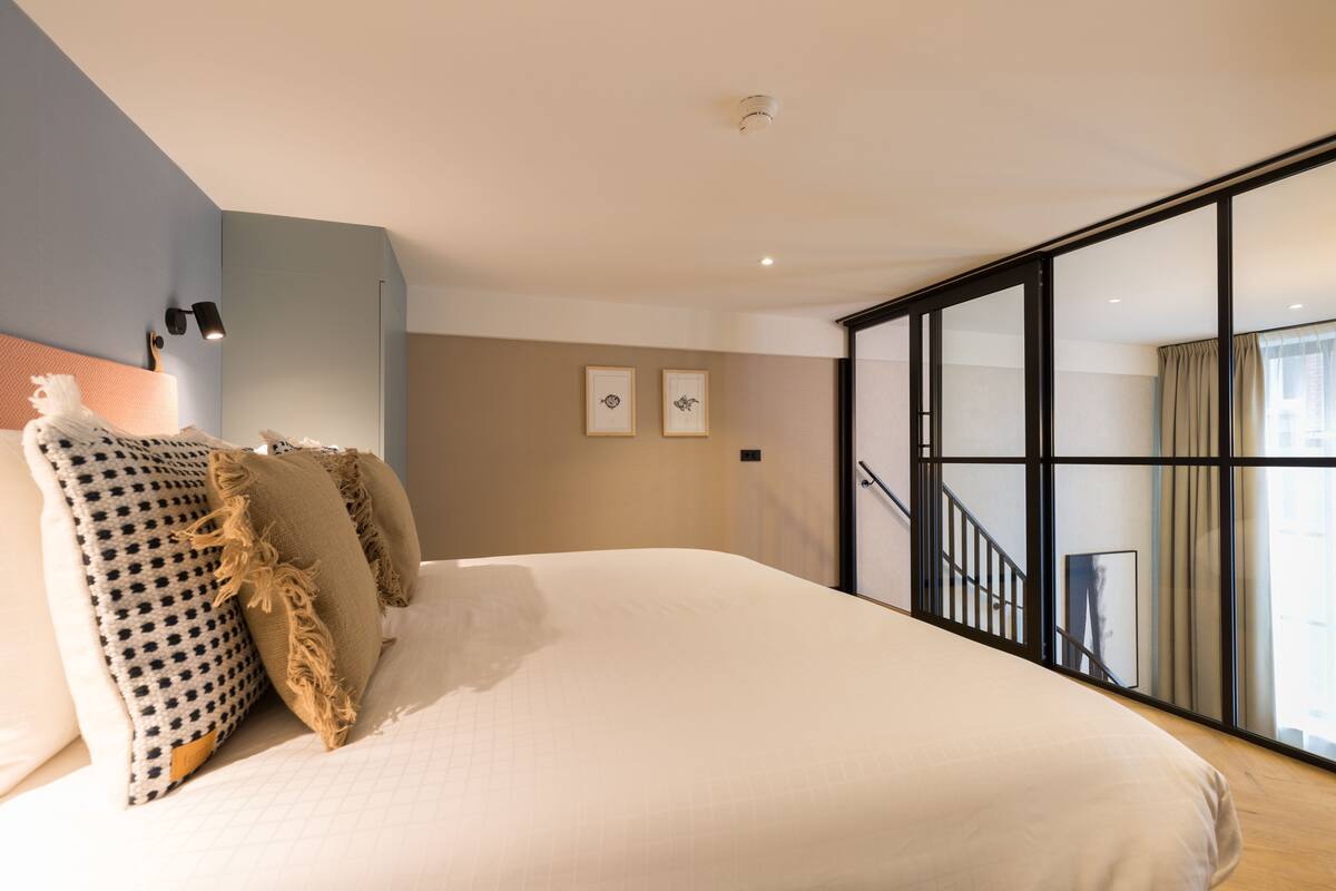 Un dormitorio con una cama grande, vistas al exterior a través de una puerta corrediza y una escalera que sube a un nivel superior.