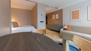 A modern hotel room with a wooden dining table, a sofa, a bed, and a view of the ocean. - Ocean House Scheveningen (The Hague)