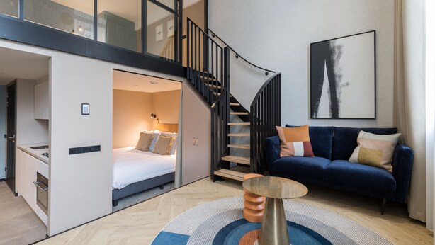 A modern apartment with a loft-style bedroom, a staircase, a blue sofa, and a large abstract painting. - Ocean House Scheveningen (The Hague)