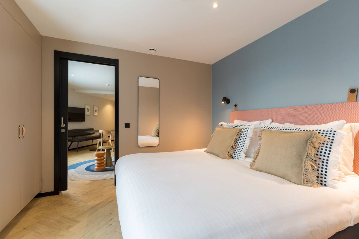 Un dormitorio moderno con una cama grande, un espejo y vistas a otra habitación.