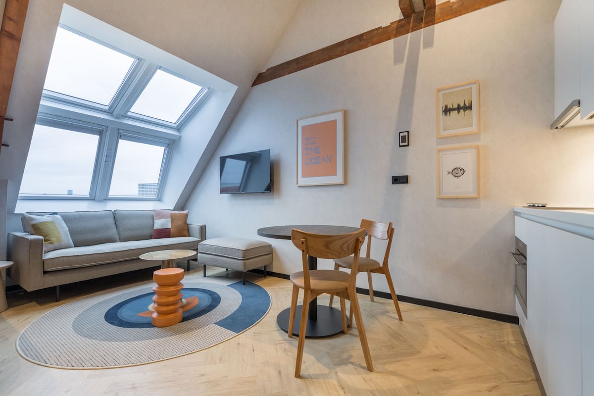 Un loft moderno con techo inclinado, un sofá, una mesa de comedor y un televisor montado en la pared.
