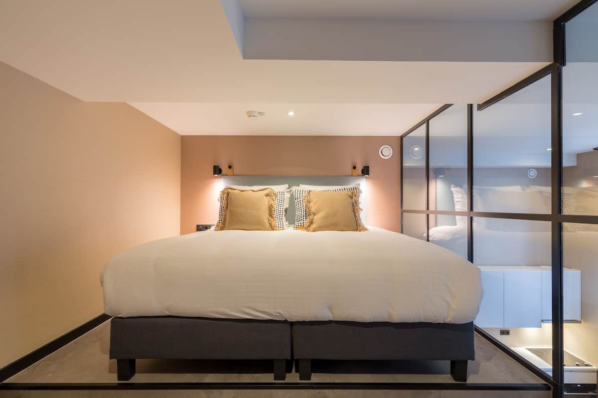 Un dormitorio moderno con una cama grande, lámparas de noche y un separador de vidrio.