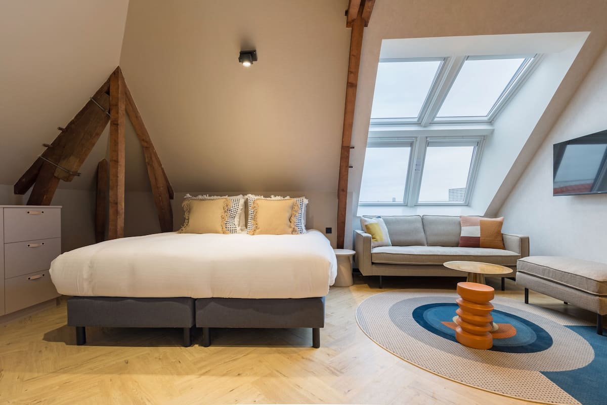 Un dormitorio moderno con una cama grande, un sofá, una mesita y un tragaluz.