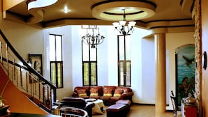 A spacious living room with a staircase, a chandelier, and a large window.