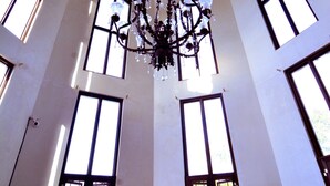 A high-ceilinged room with a chandelier, large windows, and a circular skylight.