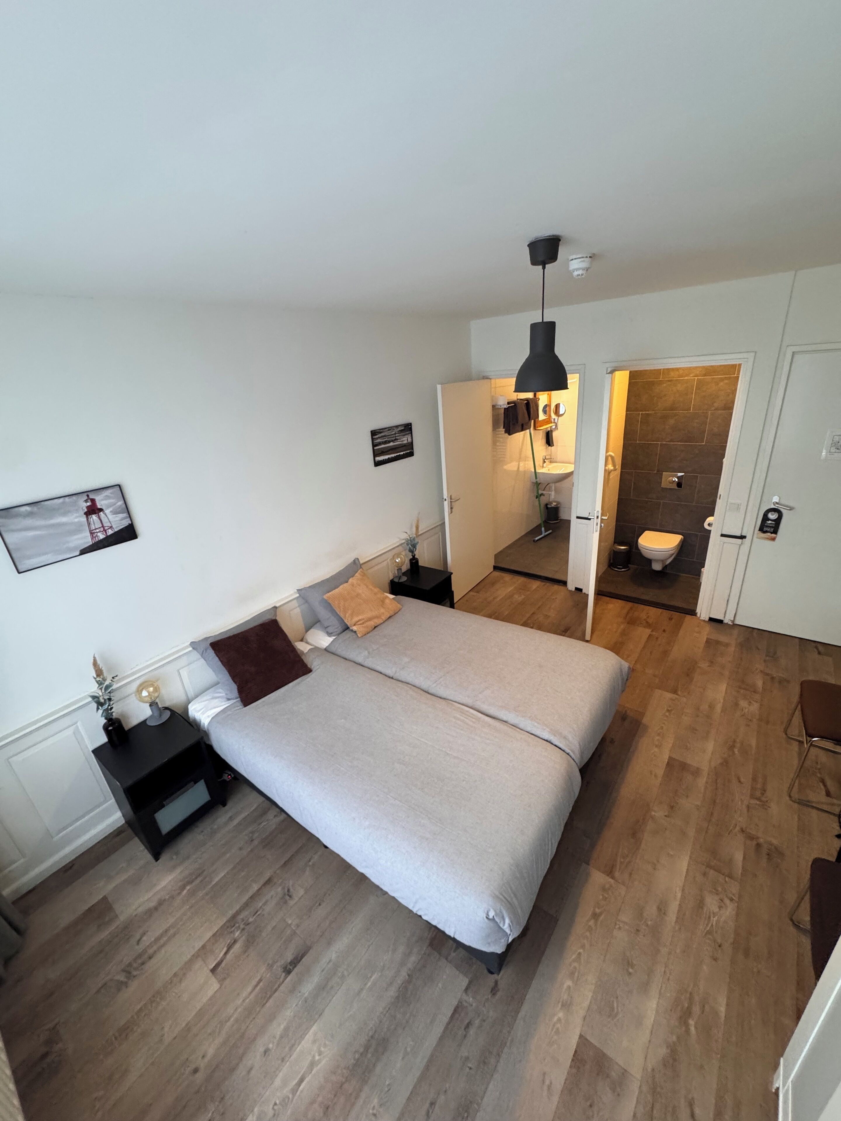 Un dormitorio moderno con cama, mesitas de noche, una lámpara colgante y un baño visible a través de una puerta abierta.