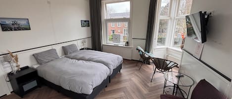 A hotel room with two beds, a TV, a chair, and a window with a view of buildings.