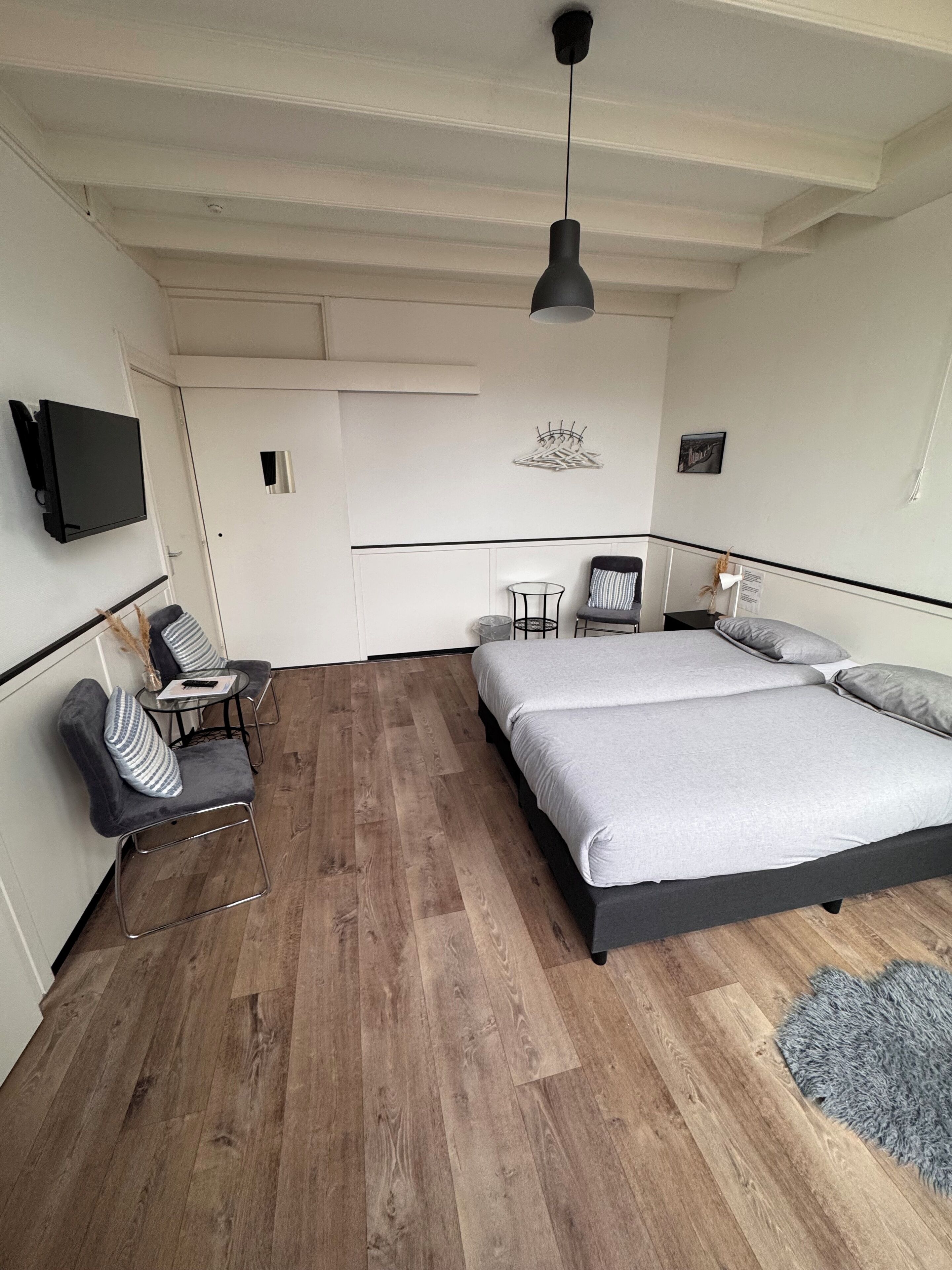 Un dormitorio moderno con una cama grande, una mesita pequeña, dos sillas, un televisor y una lámpara en el techo.