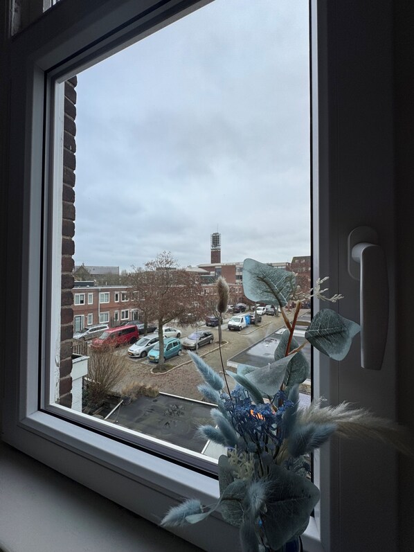Et vindue med udsigt over et boligområde, inklusive parkerede biler og en bygning med stillads.