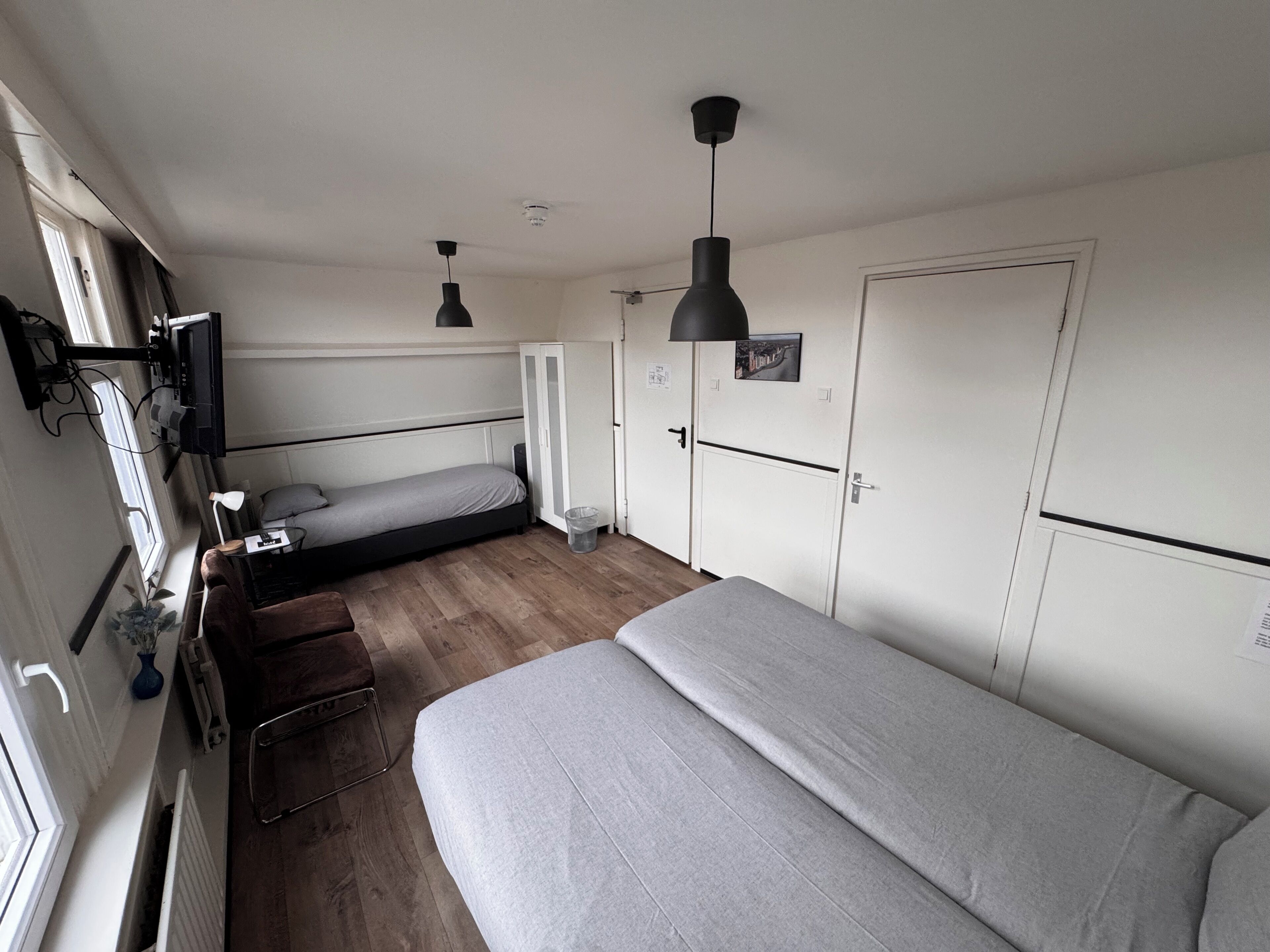 A compact room with a single bed, a desk with a chair, a wardrobe, and a television mounted on the wall.
