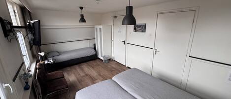 A compact room with a single bed, a desk with a chair, a wardrobe, and a television mounted on the wall.