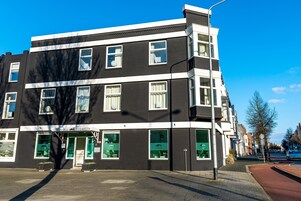 Un edificio de varios pisos con fachada blanco y negro, amplias ventanas y una entrada visible con señalización.