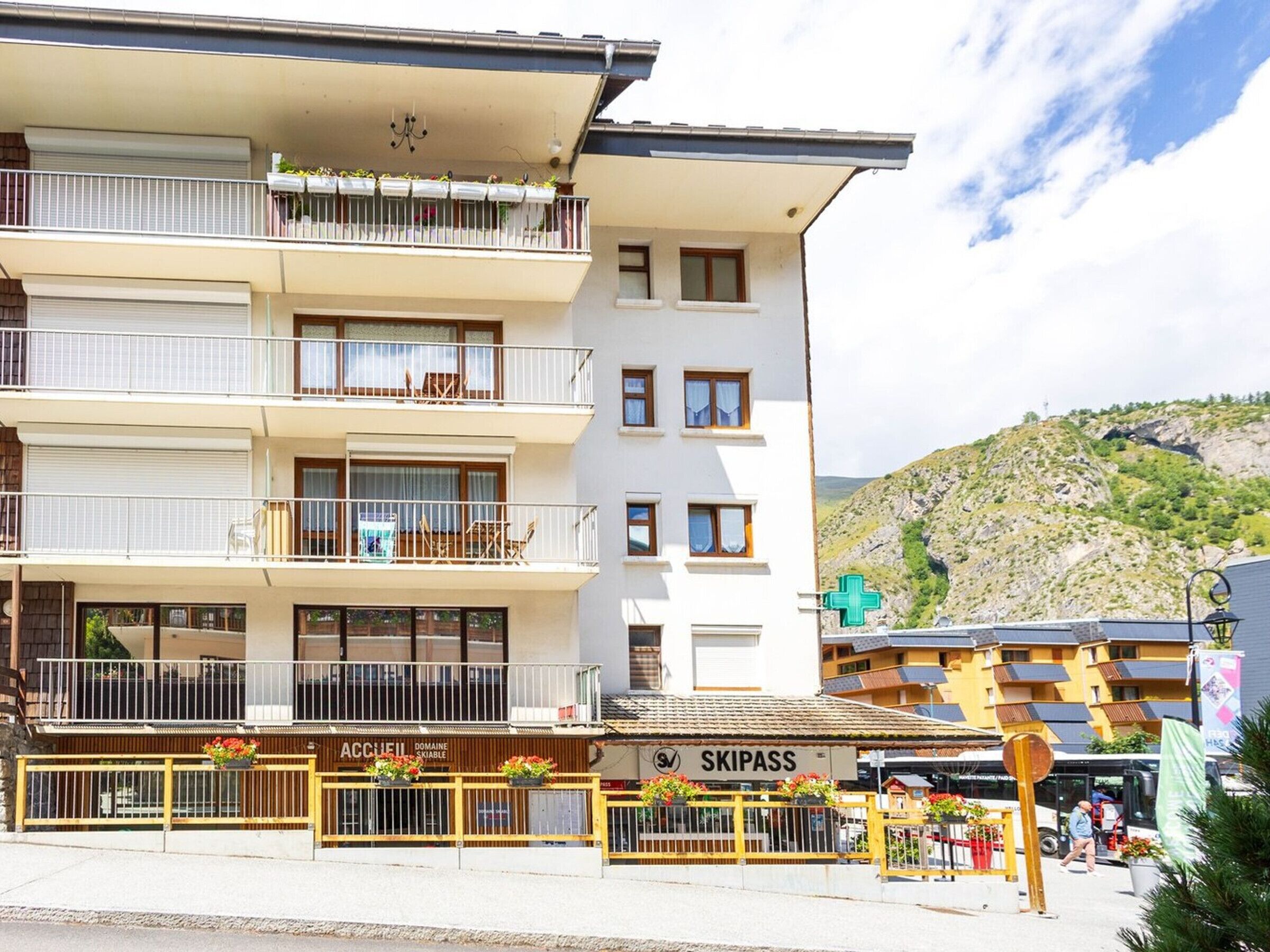 A multi-story hotel with balconies, a visible restaurant named 'SKIPASS,' and a mountainous backdrop.