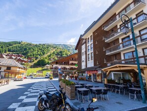 A hotel with outdoor seating, a checkered pedestrian crossing, and a mountainous backdrop.