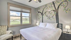 A bedroom with a large bed, a window with a view, a ceiling fan, and a wall mural of a tree. - Idyllic Gem: Screened Porch, 1/2 Mi to River! (Thermopolis)