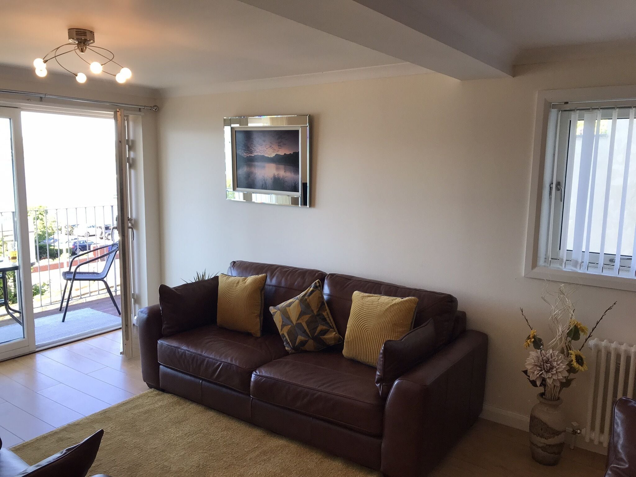 Ein Wohnzimmer mit braunem Ledersofa, einem gerahmten Bild an der Wand und einem Fenster mit Jalousien.
