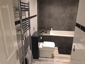 A bathroom with a modern design, featuring a bathtub, a toilet, and a towel rack.