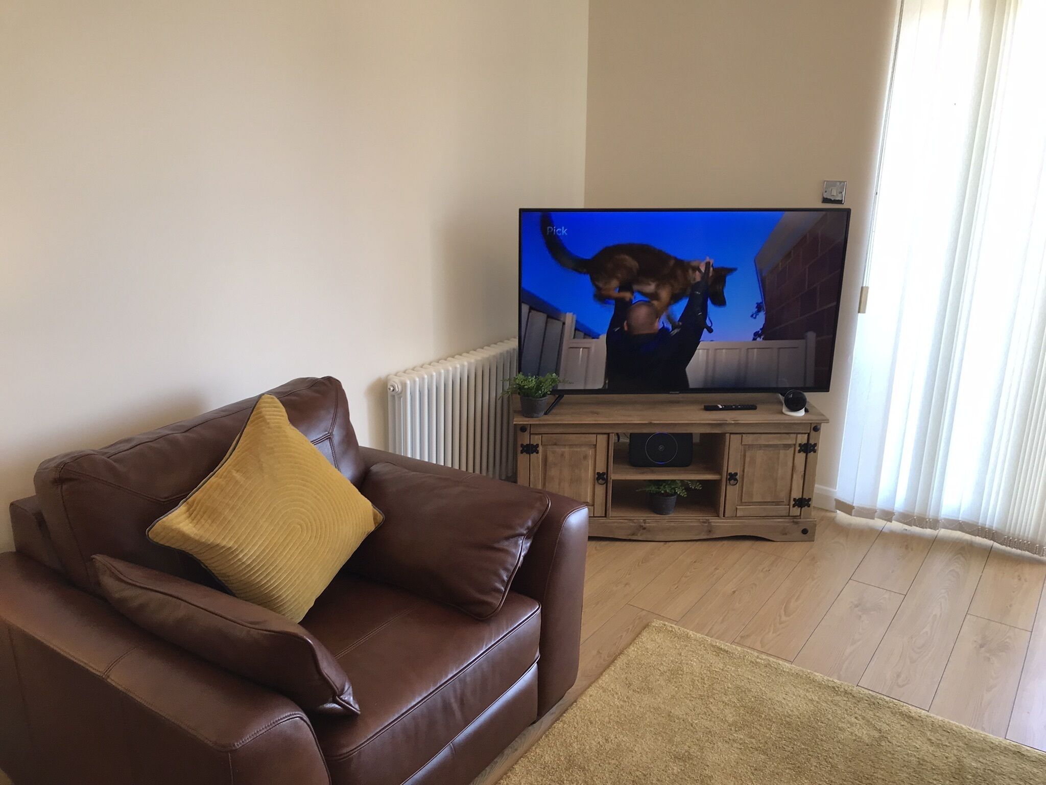 A living room with a brown leather sofa, a television, and a wooden cabinet.