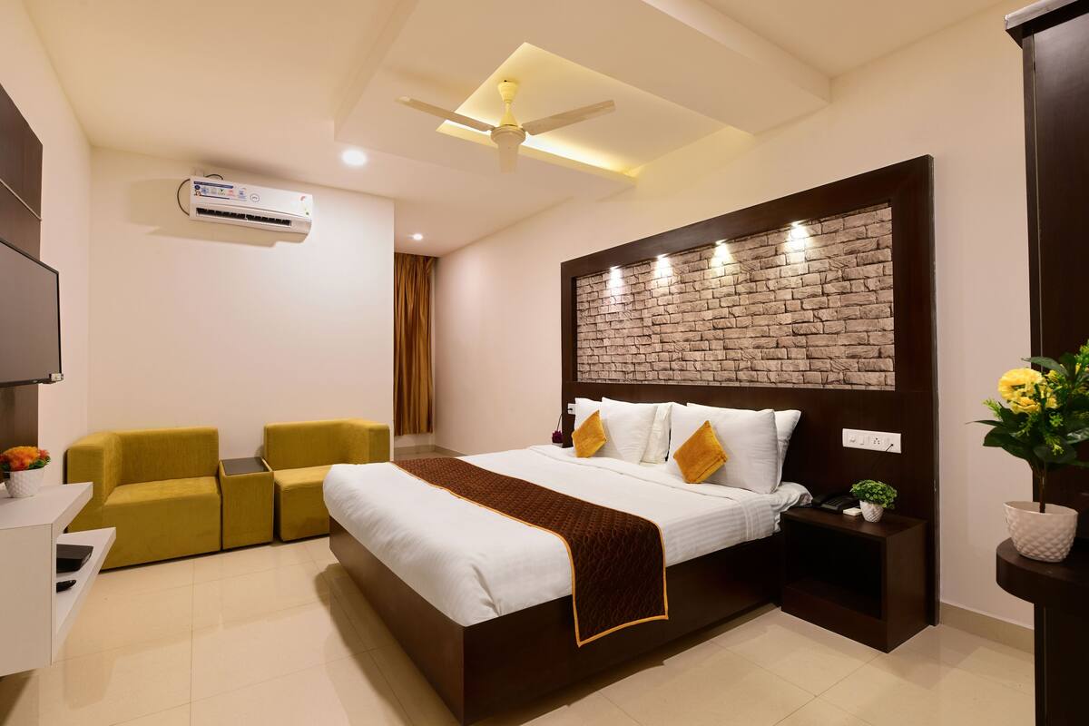 Quarto de hotel moderno com uma cama grande, um ventilador de teto, um ar condicionado, uma pequena escrivaninha com cadeira e uma parede decorativa de tijolos.