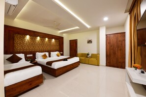 A modern hotel room with two wooden beds, a ceiling fan, recessed lighting, a wooden wardrobe, a yellow armchair, and a small table with flowers. - Hotel BV Colours By Rivido (Bengaluru)