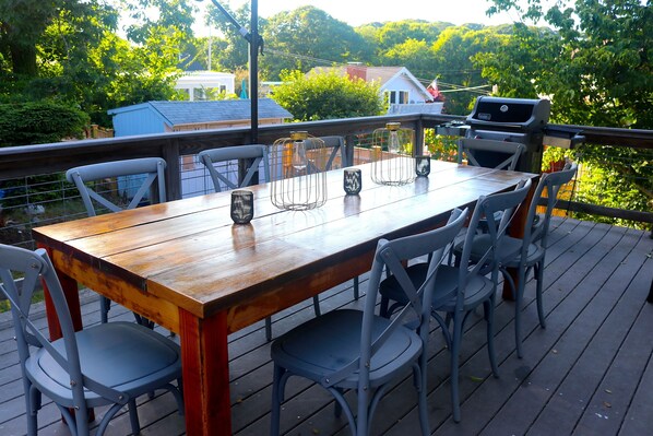 A wooden deck with a table and chairs, a grill, and a view of a house and trees.