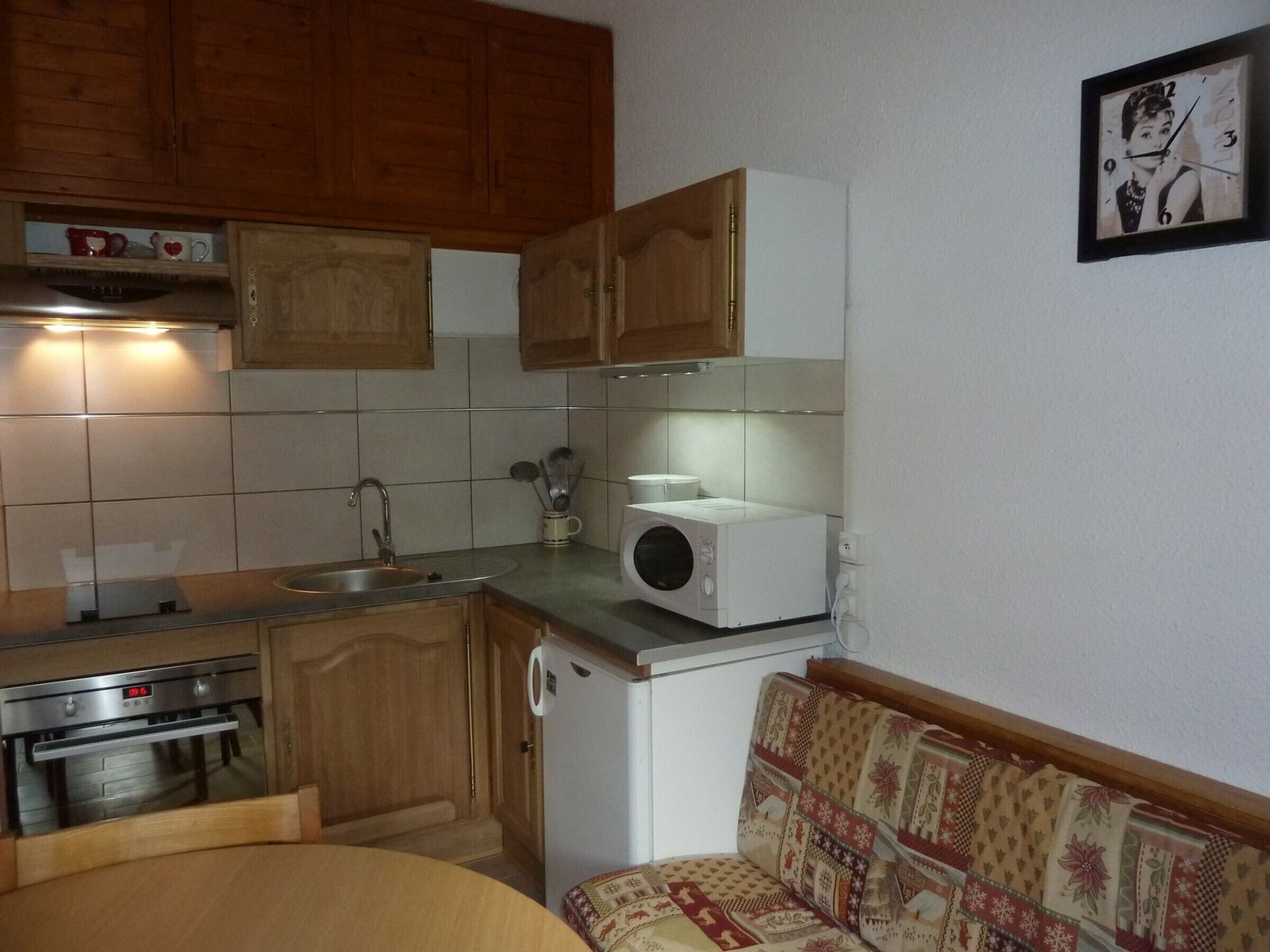 A compact kitchen with wooden cabinets, a microwave, a sink, and a built-in oven.