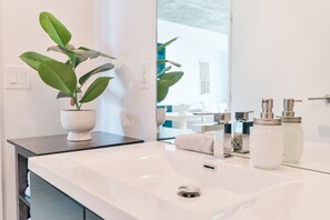 Une salle de bain moderne avec un lavabo blanc, un miroir, une plante en pot et des articles de toilette.
