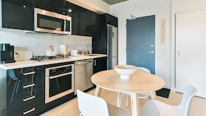 A modern kitchen with a microwave, toaster, and stove, a dishwasher, and a round table with chairs. - King Bed | DT Views | Mins to Stampede | Gym | AC (Calgary)