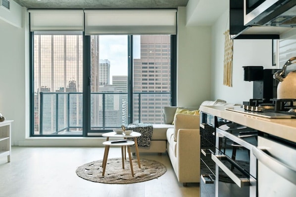 Um apartamento moderno com uma grande janela, cozinha equipada com fogão, sofá e uma pequena mesa redonda.