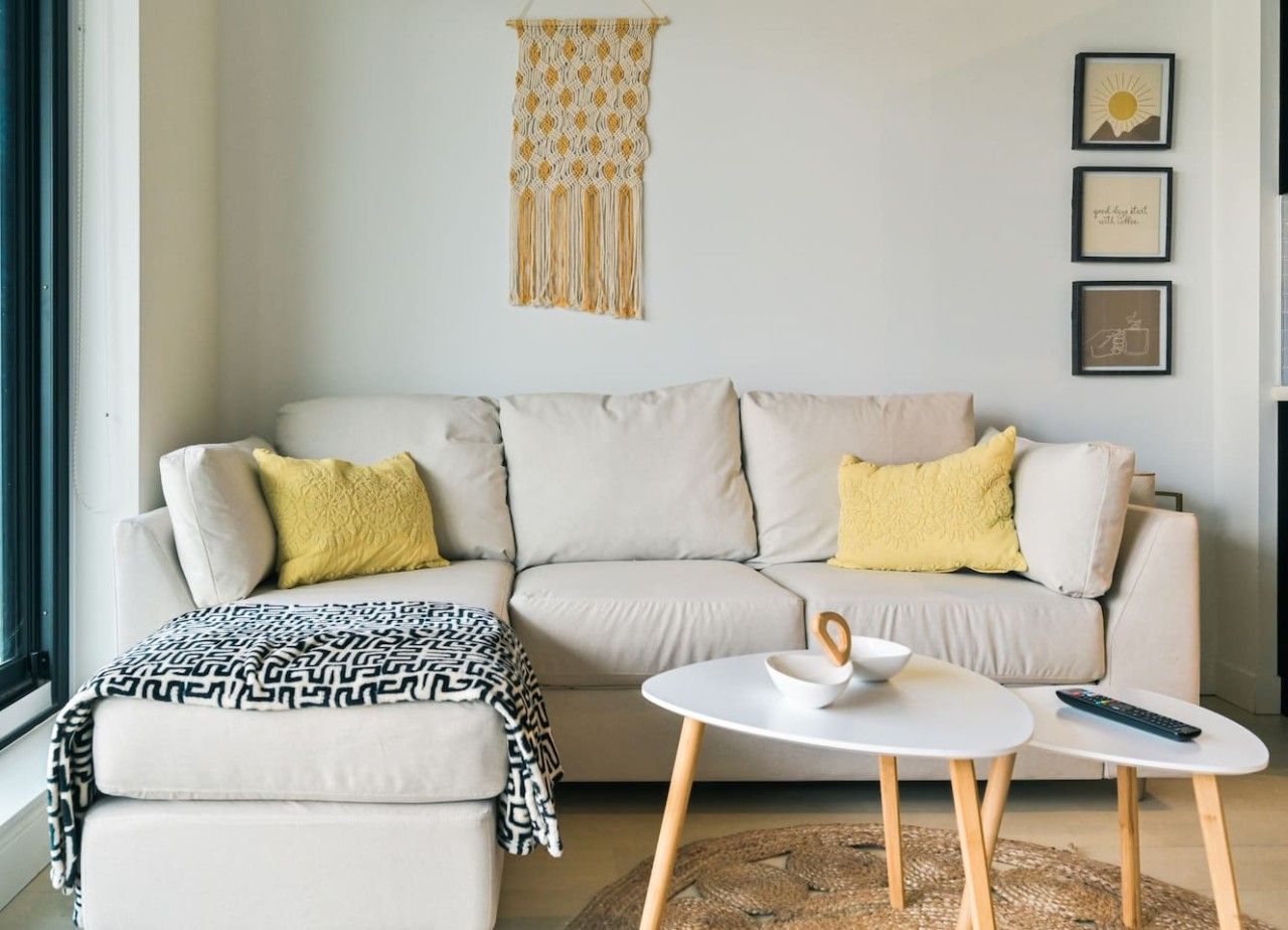 A living room with a sofa, a coffee table, and a macrame wall hanging.