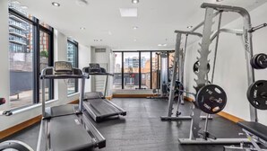 A gym with treadmills, a weight bench, and a squat rack. - King Bed | DT Views | Mins to Stampede | Gym | AC (Calgary)