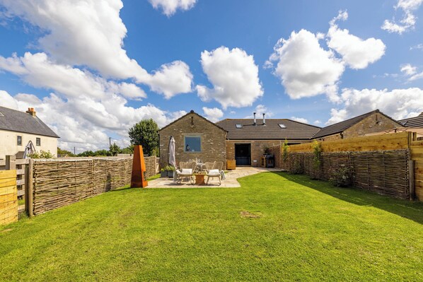 A spacious backyard with a patio area, a stone building, and a wooden fence.