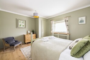 A bedroom with a bed, a chair, a dresser, and a window with curtains.