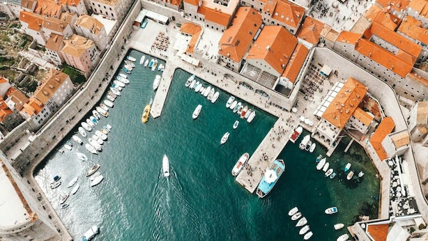 An aerial view of a marina with boats docked, surrounded by buildings with orange roofs. - Apartment Jany (Dubrovnik)