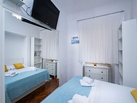 A hotel room with two beds, a TV mounted on the wall, and a painting on the wall.