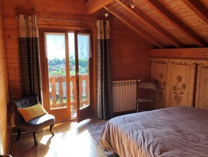 Une chambre aménagée dans une cabane en bois, avec un lit, une chaise dotée d’un coussin, un radiateur et une porte-fenêtre coulissante donnant sur l’extérieur.