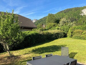 Un espace extérieur aménagé pour les repas, avec une table et des chaises, entouré d’une pelouse bien entretenue et d’une végétation dense.